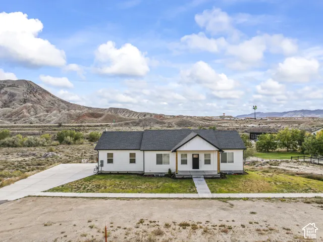Single-story residence featuring white vertical and horizontal siding, a dark asphalt shingle roof, a covered front entryway with wood-finish supports, and a concrete driveway, set against a mountainous landscape