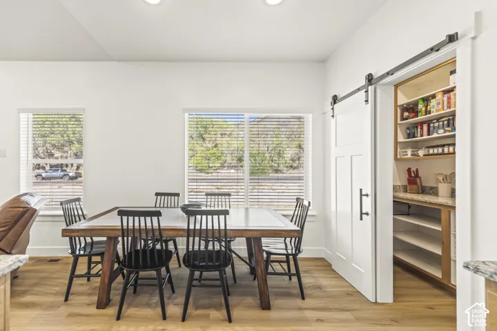 Walk-in pantry featuring stone countertops, built-in shelving, and a white sliding barn door, complemented by wood-finish flooring and windows with horizontal blinds