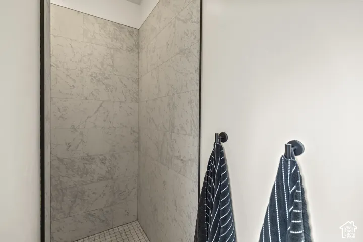 Shower enclosure featuring large-format stone-patterned wall tile, mosaic tile flooring, and matte black hardware