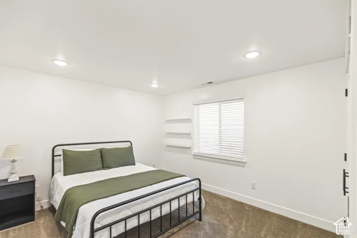 Neutral-toned interior space featuring recessed ceiling lighting, wall-mounted floating shelves, and carpeted flooring