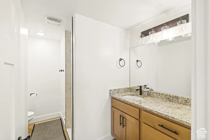 Wood-finish vanity with a stone countertop, undermount sink, matte black hardware, and an expansive wall-mounted mirror with multi-light fixture