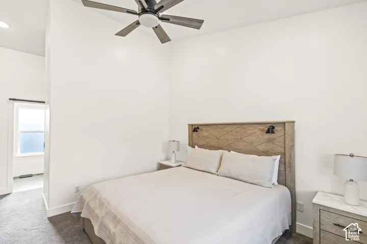 High ceiling featuring a neutral-toned multi-blade ceiling fan, wall-to-wall carpeting, and a doorway with a minimalist window