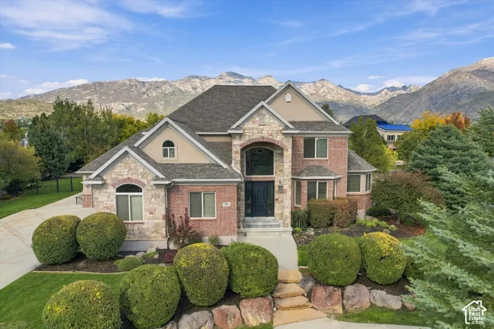 Multi-level residence featuring a brick and stone facade, arched entryway, multi-gabled roofline, and mountain backdrop