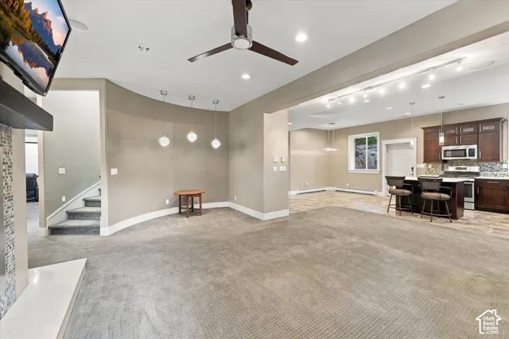 Open floor plan featuring a curved wall, multi-pendant lighting, recessed ceiling lighting, a dark-finish kitchen island with built-in cabinetry, and a fireplace surround with stone-tile detailing