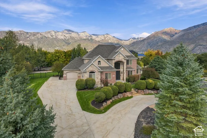 Multi-gabled brick and stone exterior, concrete driveway, attached multi-car garage, manicured landscaping, and mountain backdrop