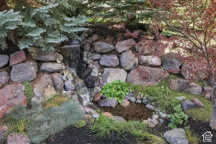 Stacked stone waterfall feature incorporating a natural rock retaining wall, ornamental shrubs, and mature evergreen plantings