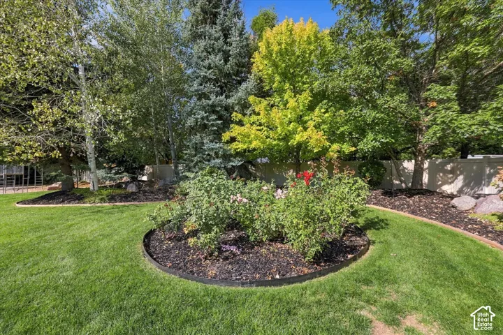 Expansive lawn area featuring mature trees, dark mulch garden beds, perennial shrubs, and a perimeter privacy fence