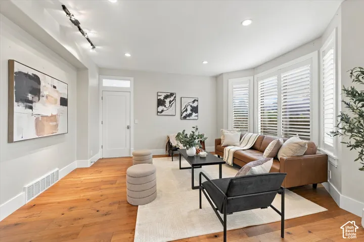 Living area featuring wood-finish flooring, bay windows with plantation shutters, recessed lighting, and adjustable track lighting