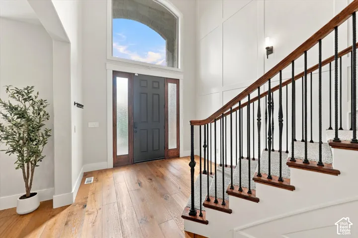 Foyer featuring wood-finish flooring, a paneled accent wall, a staircase with wood handrails and black iron balusters, a dark-toned front door with sidelights, and an arched transom window