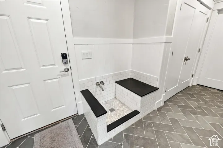 Built-in wash station featuring white subway tile surround, dark stone-finish countertops, herringbone floor tile, and a wall-mounted faucet