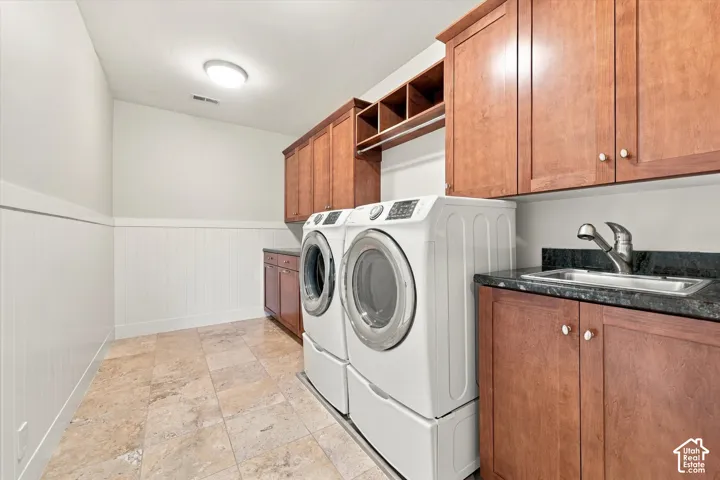 Laundry room featuring natural stone tile flooring, stained wood cabinetry, stone countertops, an integrated drop-in sink, and beadboard wall paneling