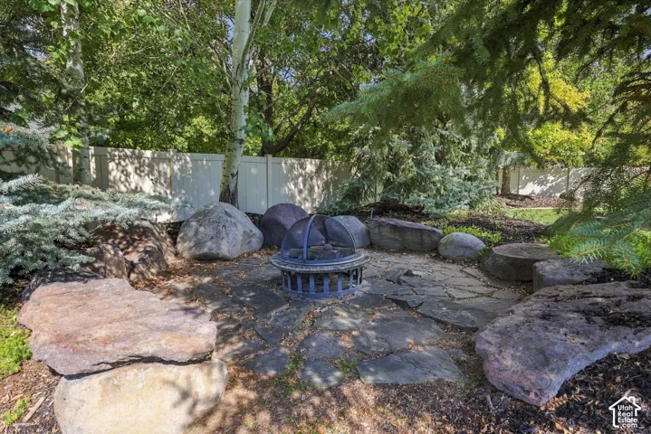 Flagstone patio featuring natural boulder accents, mature trees, and a vinyl perimeter fence