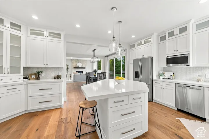 Kitchen featuring white shaker-style cabinetry with glass-front uppers, a central island with a stone-composite countertop, stainless steel appliances, and wood-finish flooring