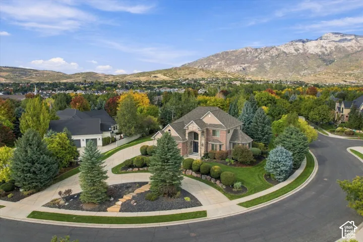 Multi-level brick and stone exterior featuring an arched entryway, expansive corner lot, curved concrete driveway, and mature landscaping set against a mountain backdrop