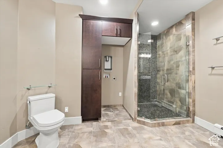 Bathroom featuring large-format tile flooring, a glass-enclosed shower with pebble-finish flooring and tile surround, custom dark wood-finish cabinetry, and recessed ceiling lighting