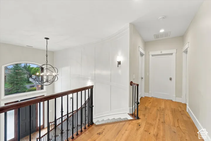 Curved wall featuring white wainscoting, wood-finish flooring, metal orb chandelier, and wrought iron staircase railing