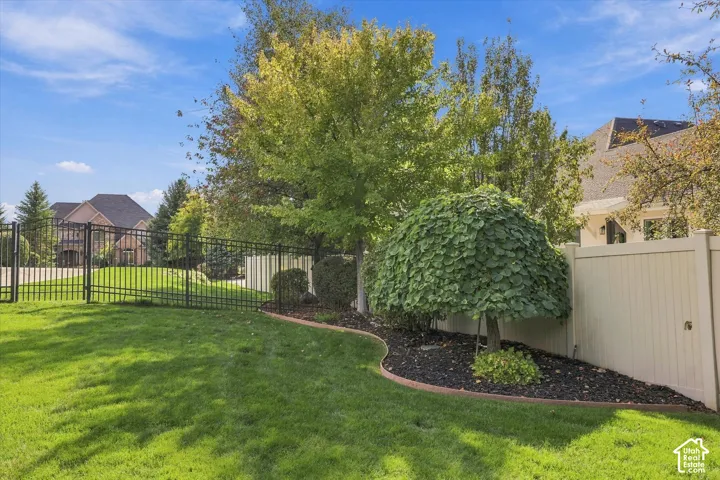 Backyard featuring a manicured lawn, perimeter metal fencing, solid-panel privacy fencing, and mature landscaping with defined mulch beds