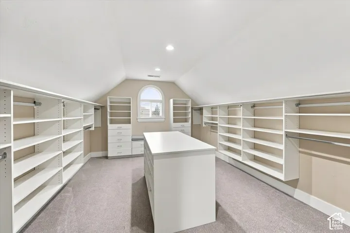 Custom dressing room featuring extensive white built-in shelving, integrated storage drawers, a central island, recessed lighting, and an arched window