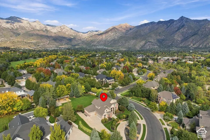 Aerial perspective of a multi-level residence featuring a multi-pitched roof, brick and stone exterior cladding, and a concrete driveway, set against a prominent mountain backdrop