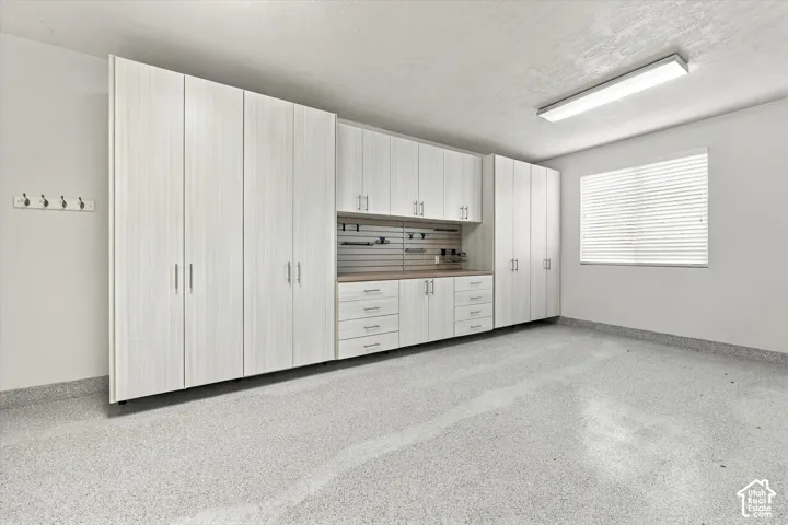 Garage featuring light-toned cabinetry with vertical wood-grain finish, integrated slat wall organization system, neutral speckled epoxy flooring, and linear overhead LED lighting