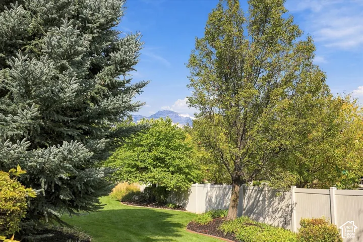 Backyard grounds featuring a manicured lawn, established landscaping, mountain backdrop, and composite privacy fencing
