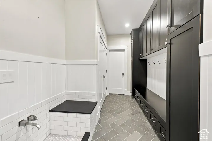 Built-in charcoal cabinetry with integrated bench seating, herringbone tile flooring, beadboard wall paneling, and a wash station featuring a wall-mounted faucet with subway tile surround