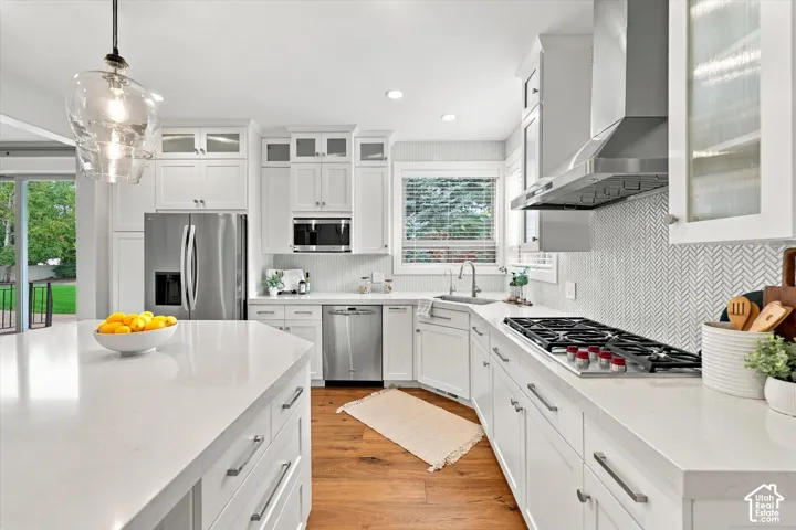Kitchen featuring white cabinetry, quartz countertops, stainless steel appliances, a herringbone-patterned tile backsplash, and wood-finish flooring