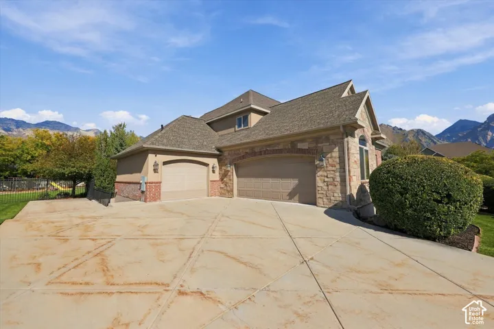 Exterior featuring stone and brick masonry, multi-car garage, expansive concrete driveway, and mountain backdrop
