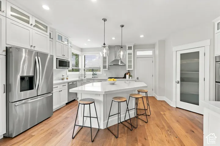 Kitchen featuring shaker-style cabinetry, a central island with quartz countertops, stainless steel appliances, pendant lighting, and wood-finish flooring