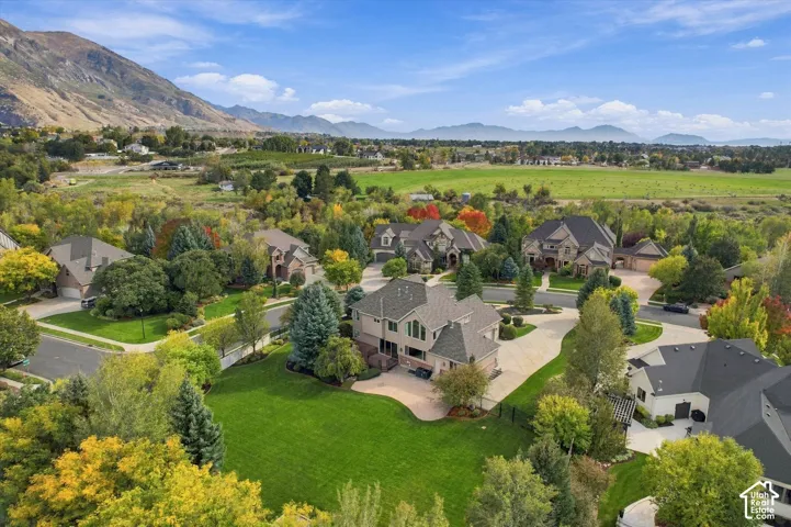 Aerial perspective of a multi-story residence featuring a paved patio, expansive lawn, mature landscaping, and mountain backdrops