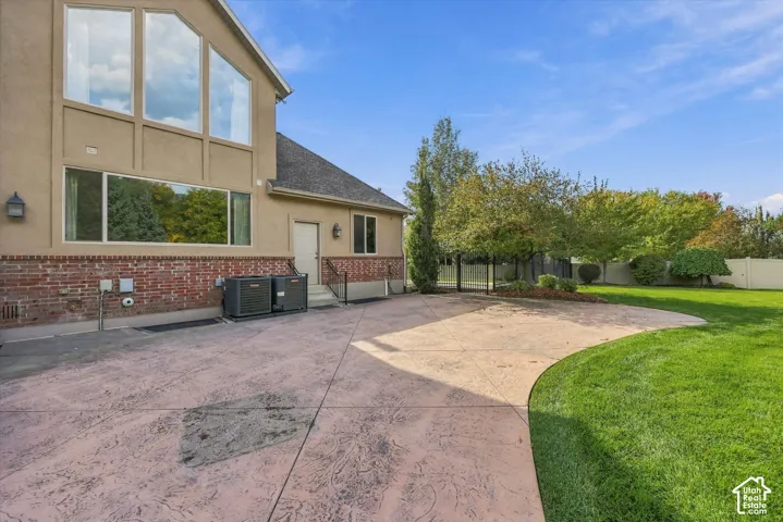 Stucco and brick exterior featuring a stamped concrete patio, multi-pane windows, and a landscaped lawn with mature trees