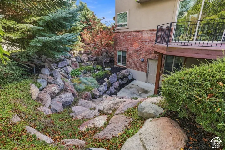 Exterior featuring brick masonry, tiered boulder retaining walls, concrete ground-level patio, and elevated deck with black metal railing