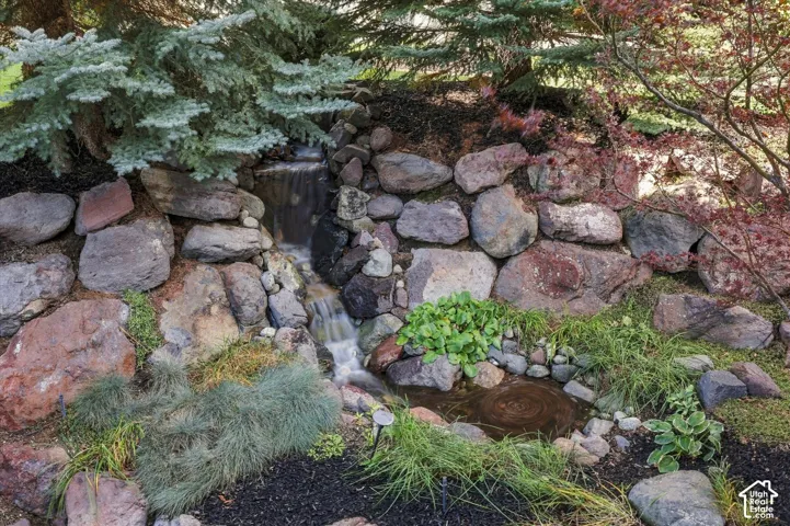 Tiered stone retaining wall with a cascading water feature, integrated rock pond, and mature evergreen and ornamental landscaping