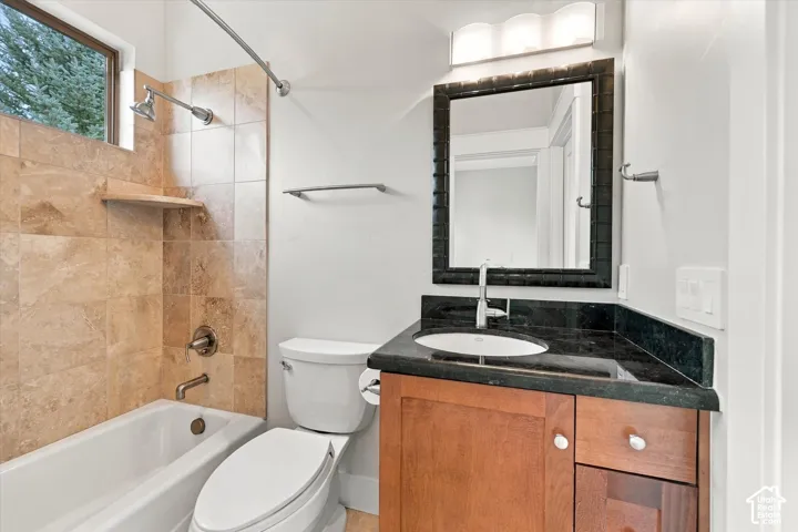 Bathroom featuring a vanity with dark stone countertop, an integrated sink, tile-surround bathtub, and a framed mirror