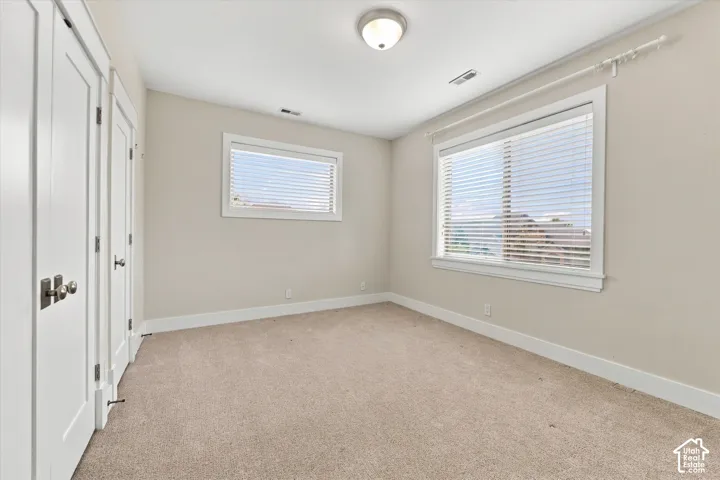 Neutral interior room featuring neutral carpeting, two windows with horizontal blinds, white-painted wood trim, and dual-door closet storage