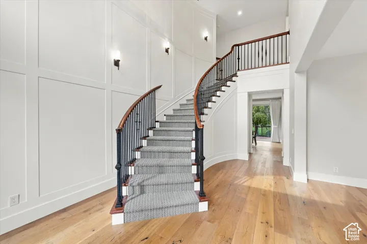 Grand foyer featuring a curved staircase with metal balusters and wood handrail, high-ceiling wall paneling, and wood-finish flooring