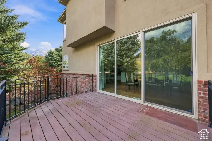 Elevated deck featuring wood-finish flooring, black metal railing, brick masonry exterior accents, and large sliding glass door entry