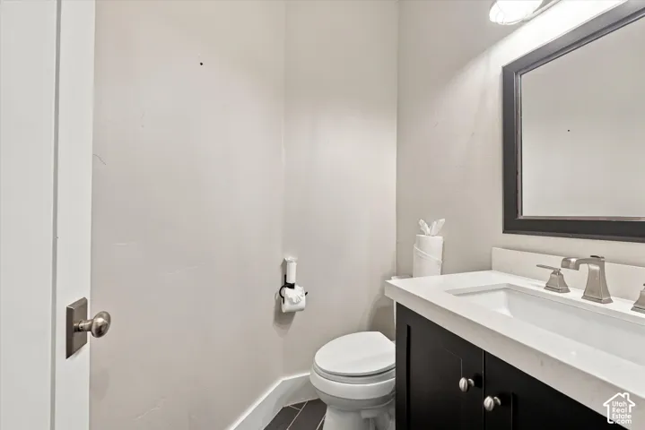 Dark cabinetry vanity with a stone countertop, integrated sink, brushed metal faucet, framed mirror, and charcoal tile flooring