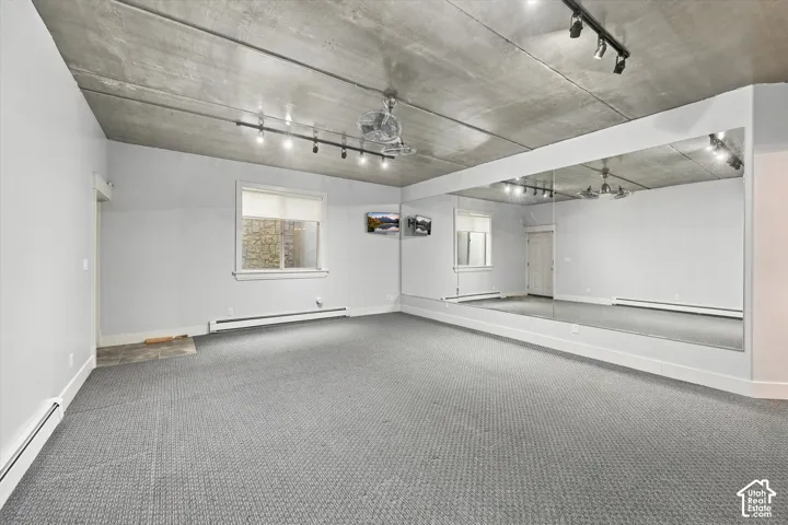 Exposed concrete ceiling with mounted track lighting, wall-to-wall mirrored surfacing, and neutral carpeting