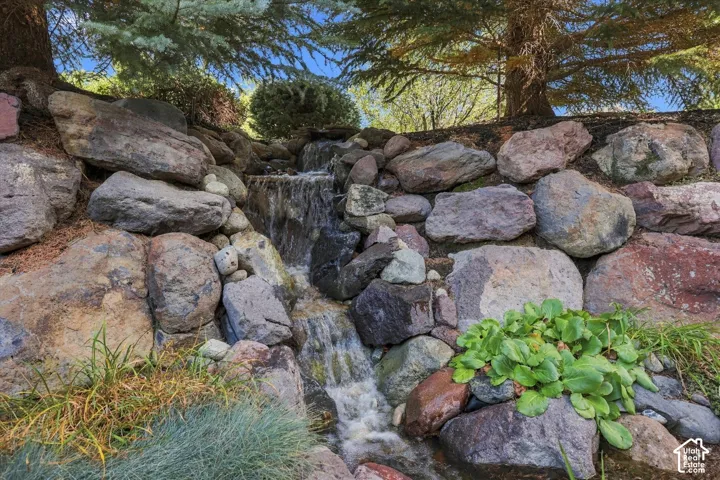 Custom landscape feature incorporating natural stacked boulders and a cascading water element surrounded by mature coniferous trees and perennial plantings