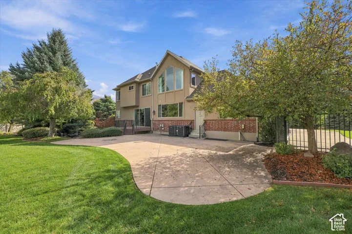 Two-story exterior featuring a brick and siding facade, expansive stamped concrete patio, multi-pane triangular windows, and mature landscaping