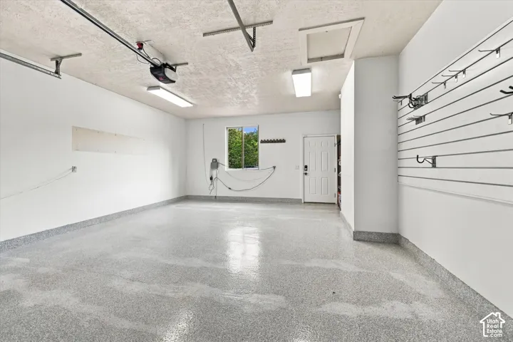 Multi-car garage featuring epoxy-finished flooring, slat wall storage system, fluorescent lighting, and an access door