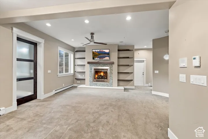 Fireplace featuring decorative tile surround, stone hearth, and dark wood mantel, flanked by built-in floating shelves, recessed ceiling lighting, ceiling fan, and frosted glass paneled door