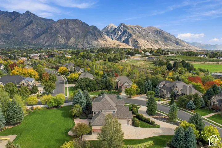 Aerial perspective of a multi-level residence featuring a multi-car garage, stone-and-stucco exterior, expansive manicured lawn, and mountain backdrop