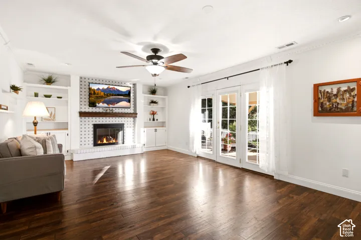 Living area featuring wood-finish flooring, a fireplace with a wood mantel, built-in shelving, crown molding, and glass-paneled French doors
