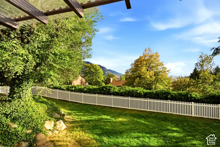 Backyard featuring a white picket fence, natural rock landscaping, manicured lawn, and overhead pergola structure