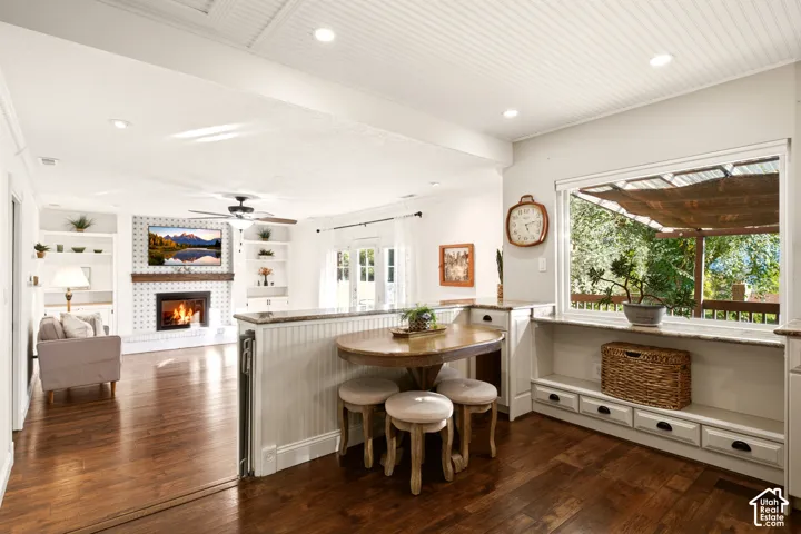 Open-concept interior featuring wood-finish flooring, beadboard ceiling detailing, stone-surround fireplace, built-in shelving, and custom cabinetry with stone counters