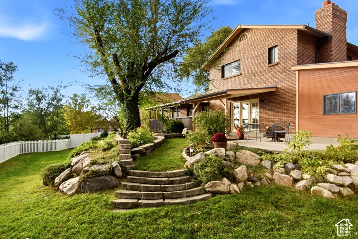 Multi-level brick exterior featuring a stone chimney, tiered natural stone retaining walls, stone stairs, and a concrete patio