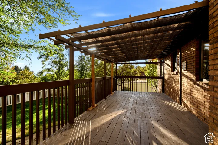 Covered wood deck featuring a lattice-style pergola, vertical baluster railings, and brick exterior wall