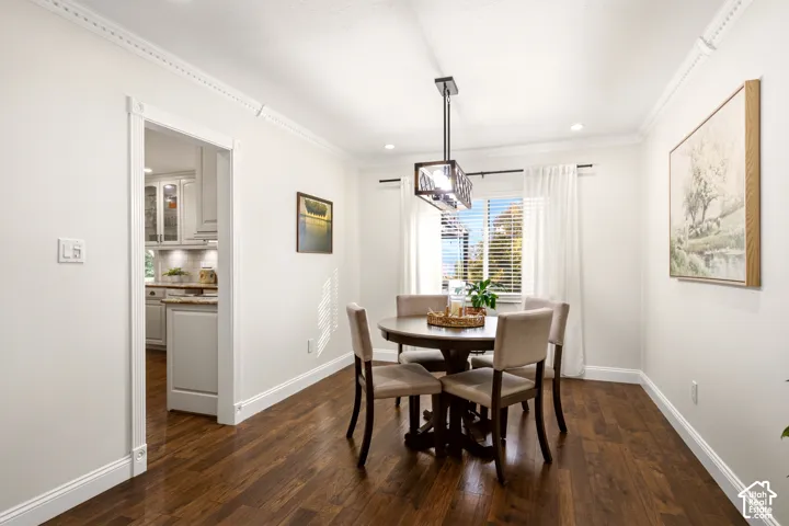 Dining area featuring dark wood-finish flooring, crown molding, and a modern rectangular pendant light fixture